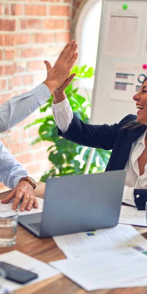 Two people in an office doing a high five and smiling.