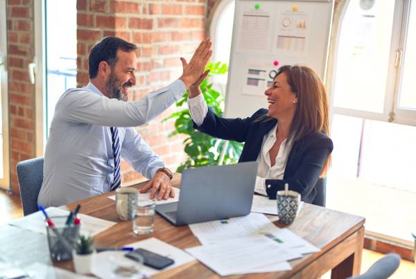 Two people in an office doing a high five and smiling.